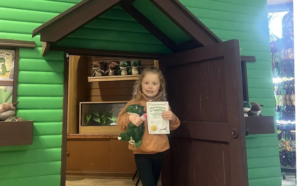 A child holding a plush dinosaur and Certificate of Adoption at the ROARR! STORE