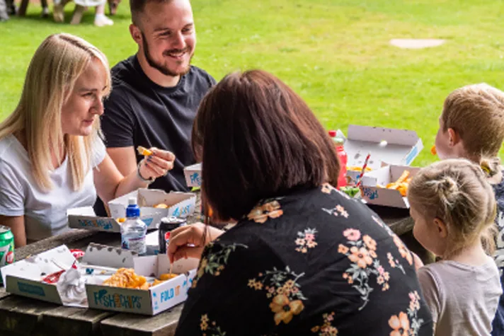 A family tucking into fish and chips at a picnic bench