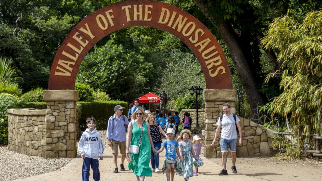 A family walking through the Valley of the Dinosaurs entrance archway at ROARR! on a sunny day